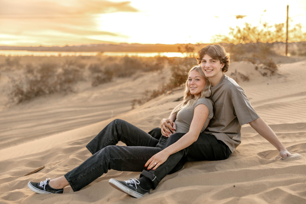  Intimate moment between a couple in the Hidden Dunes, with a desert sunset in the background.