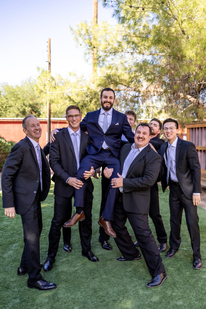 Groom celebrating with groomsmen during wedding portraits at Schnepf Farms in Queen Creek, Arizona
