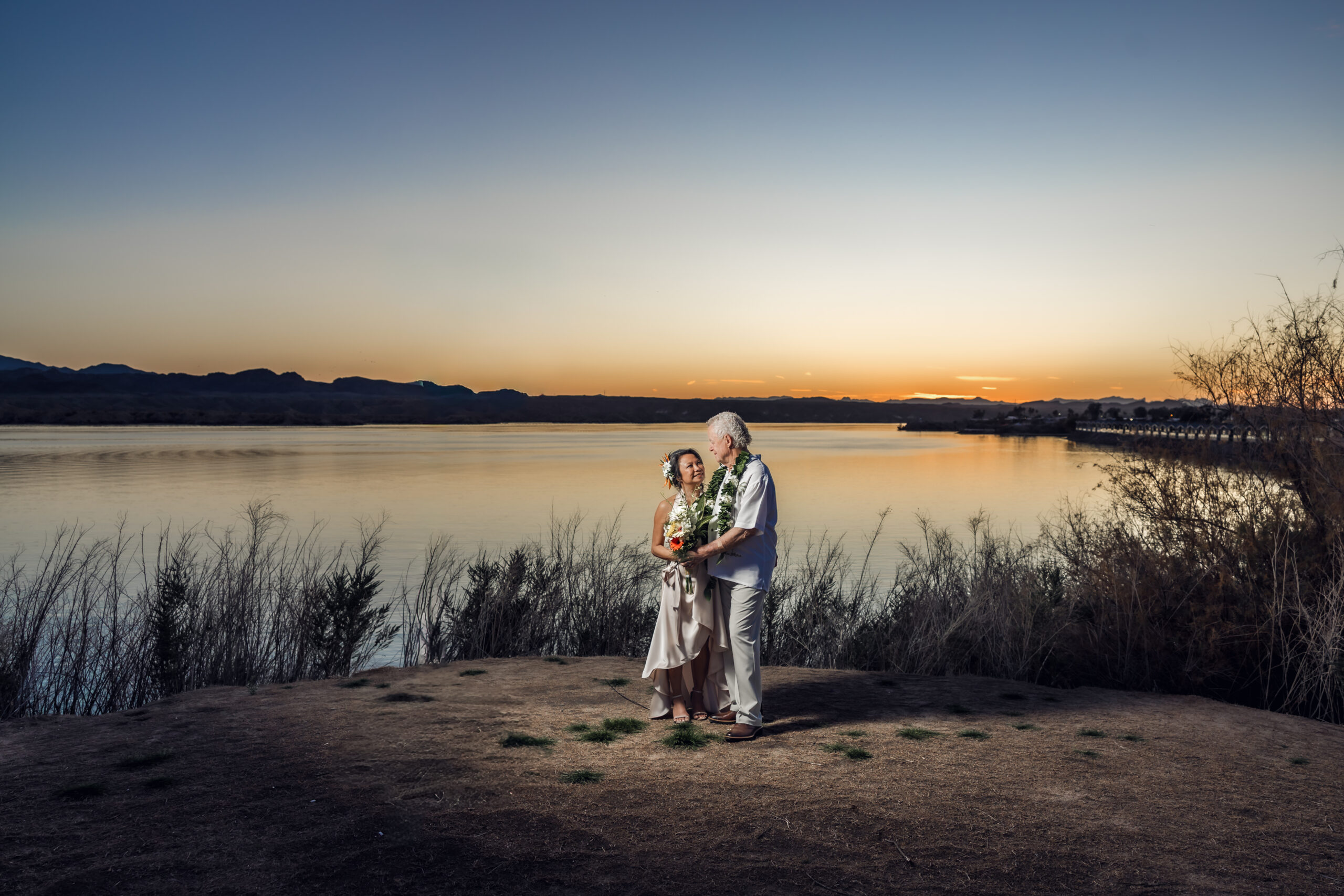 Couple embracing at sunset at Nautical Beachfront Resort in Lake Havasu, Arizona with glowing sky and mountain silhouettes