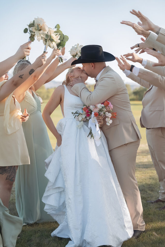 atie and Darren kiss beneath raised bouquets and hands from their wedding party.